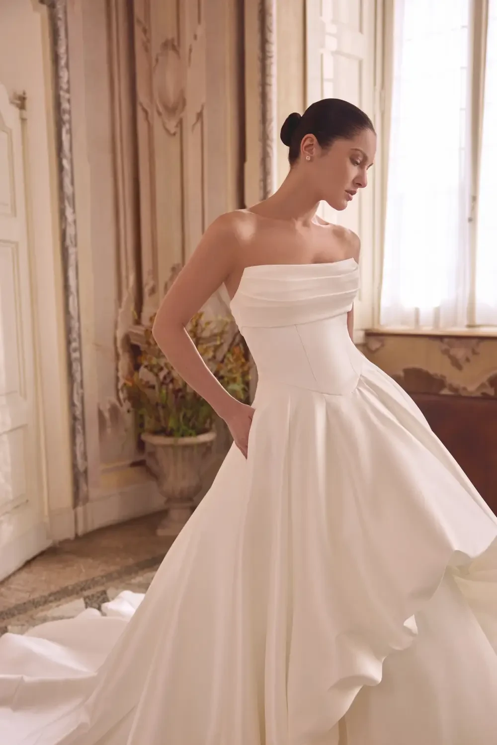A woman wearing a strapless white gown, standing gracefully in an elegant interior with soft lighting.