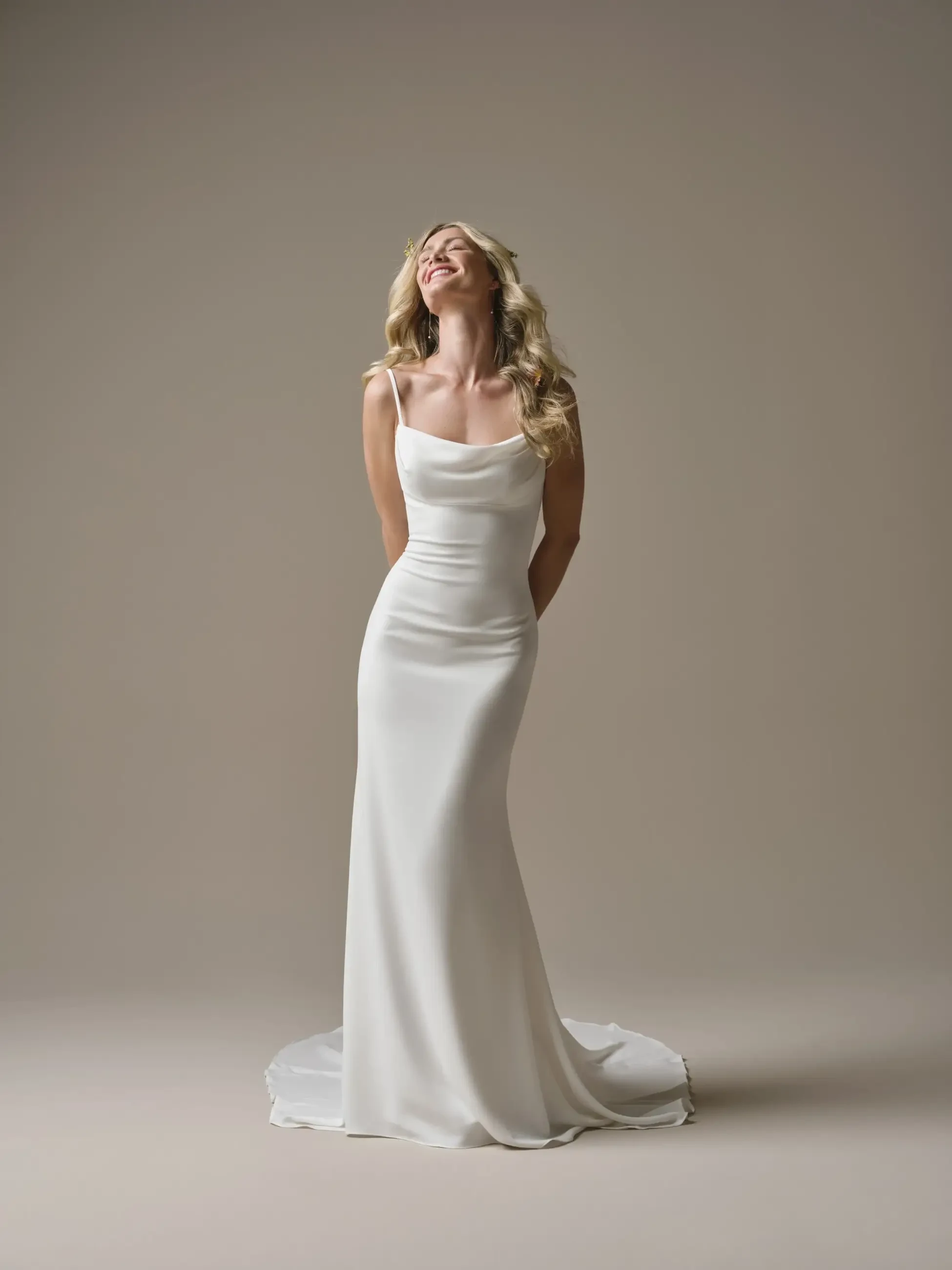 A woman in a white evening gown smiles while standing against a neutral background.