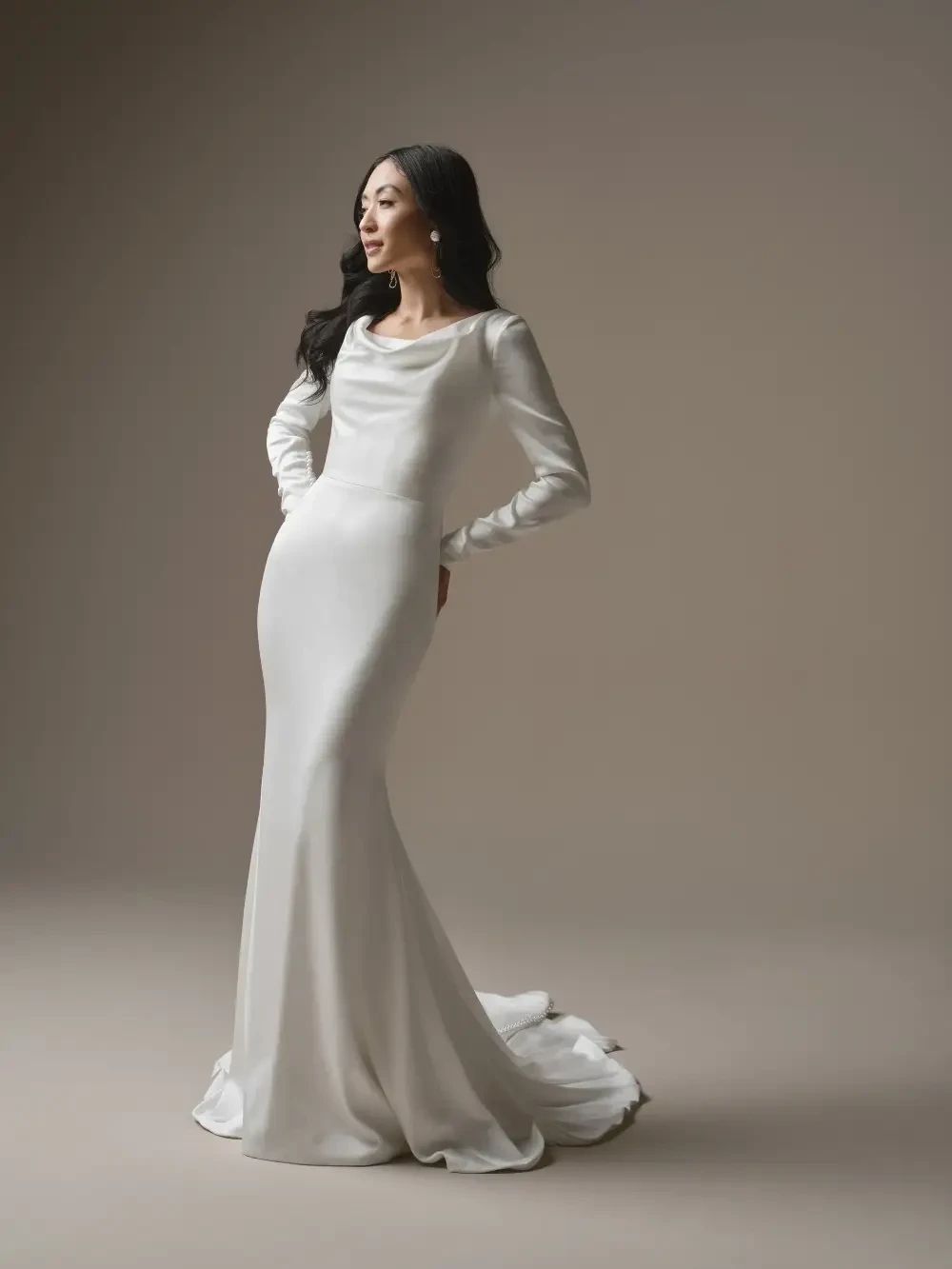 A woman in a sleek, fitted white dress with long sleeves, standing elegantly against a neutral background.