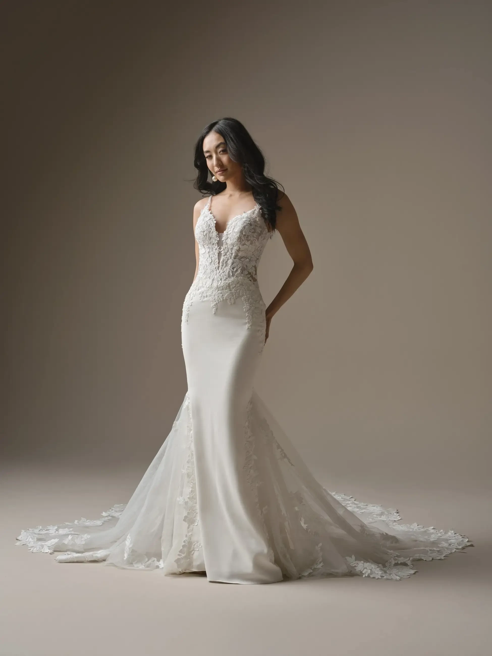 A woman wearing a form-fitting wedding dress with intricate detailing on the bodice, standing against a neutral background.