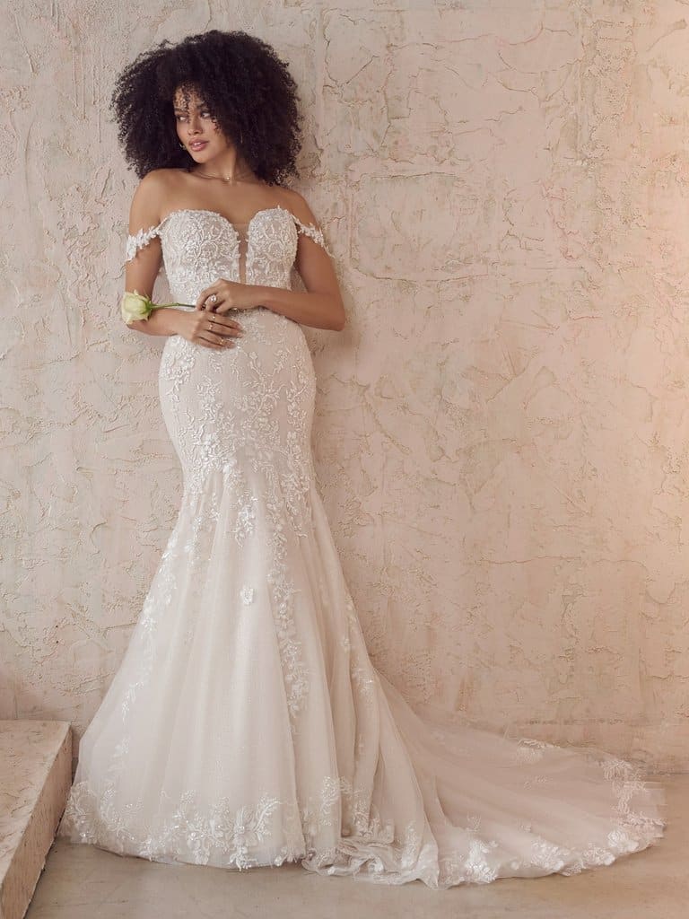 Woman leaning against a wall in off-the-shoulder wedding gown