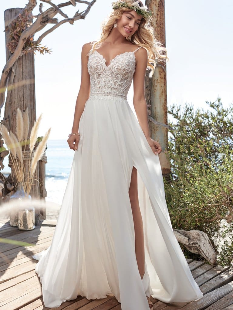 Blonde haired bride standing outside on the beach wearing flowy wedding dress