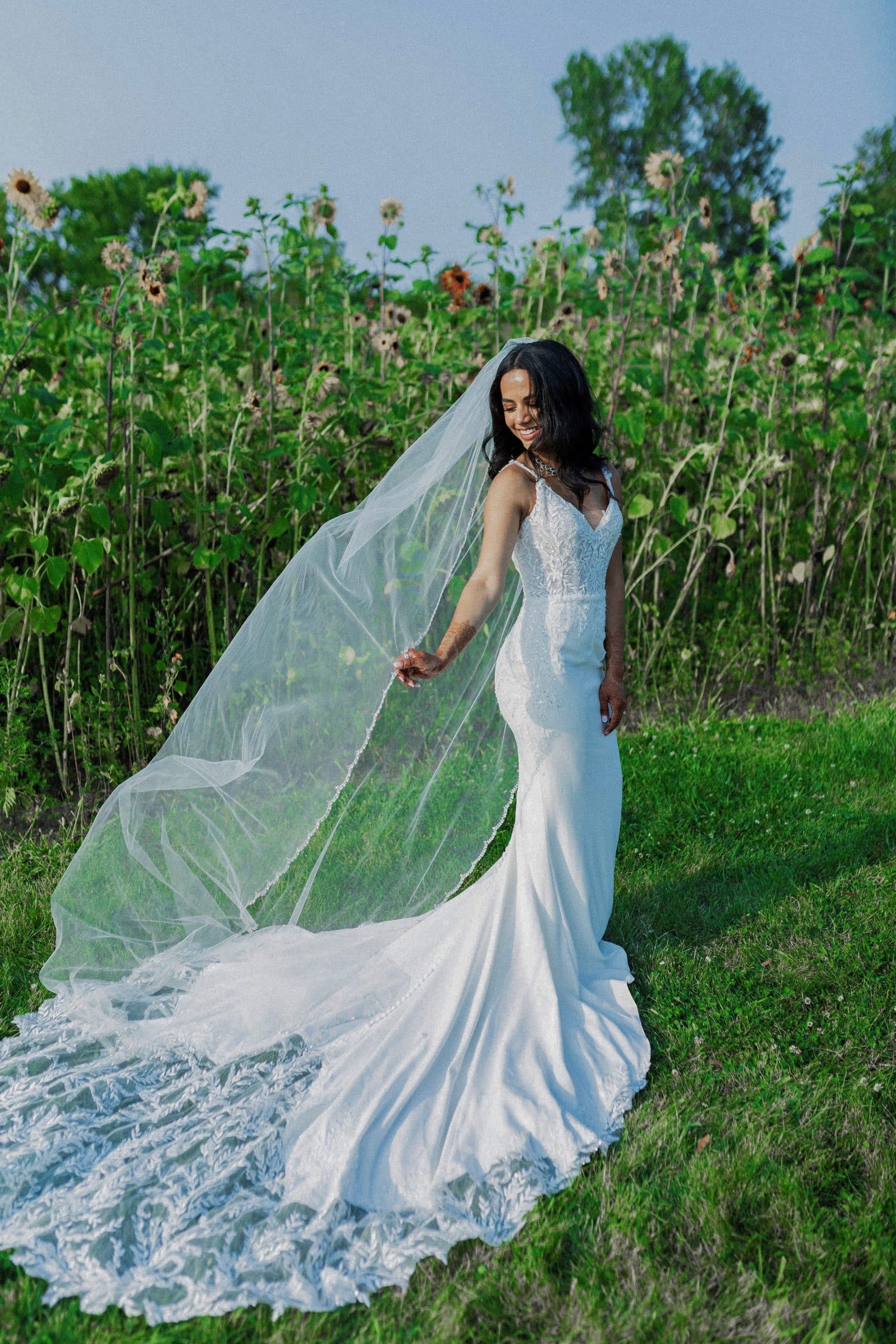 Bride standing outside in a flower field with long veil and train