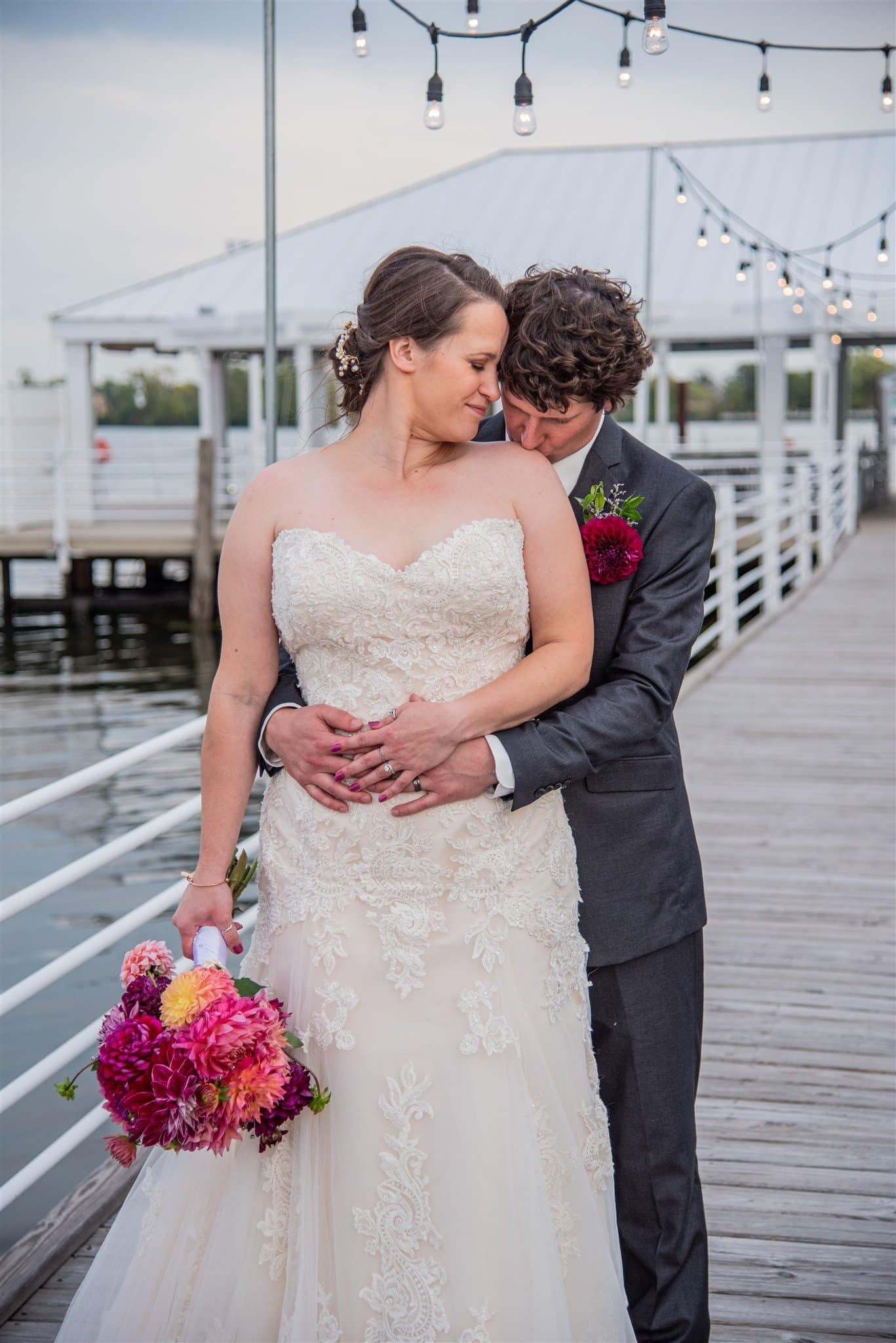 Bride and groom standing outside groom kissing bride's shoulder