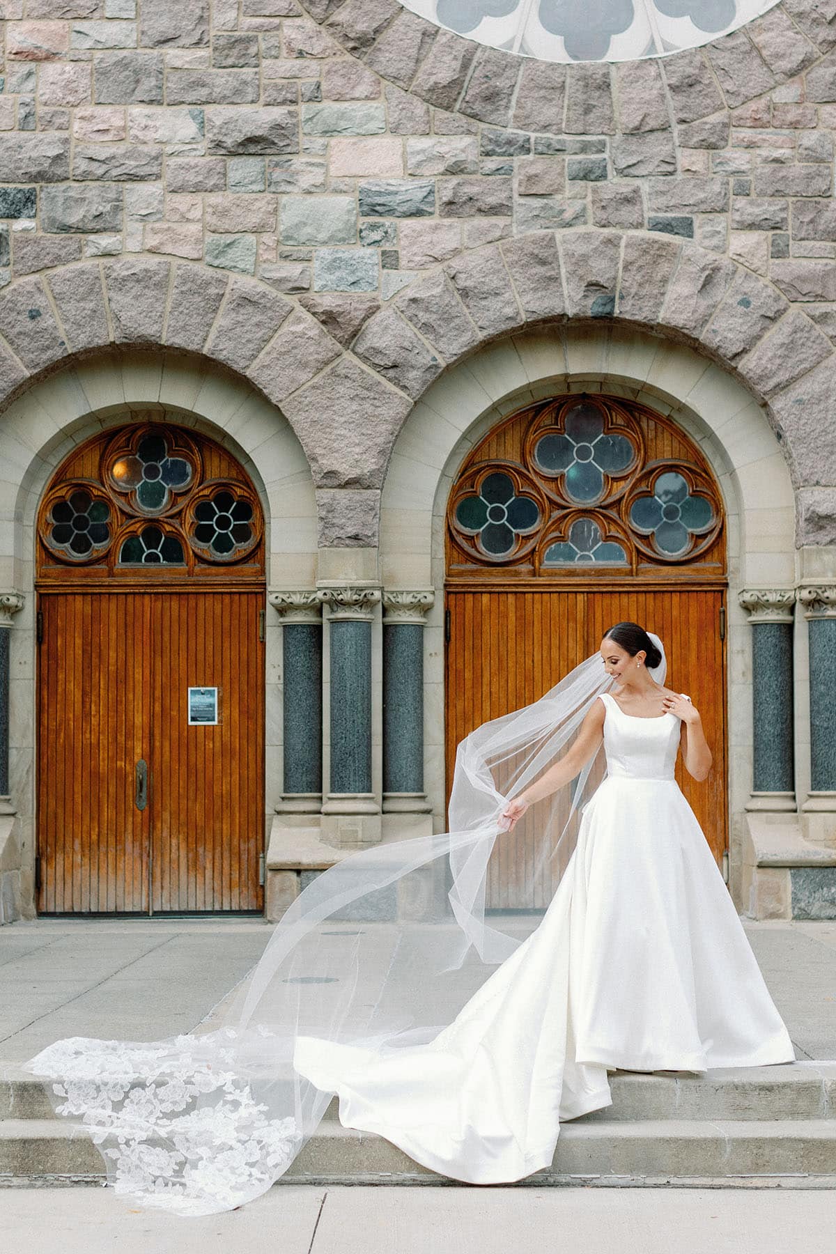 Bride standing in front of a church with ballgown and long veil blowing in the wind