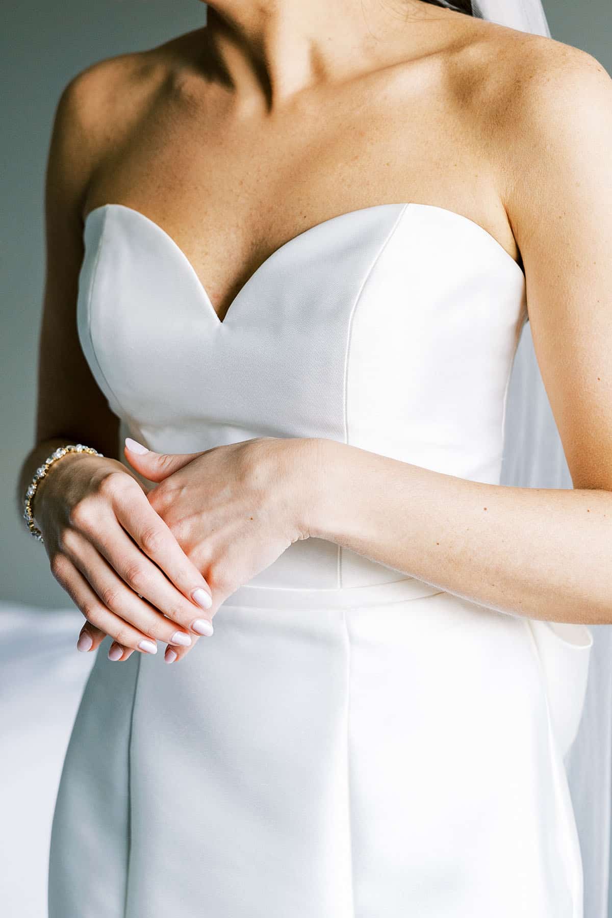 Bride standing with hands overlapping wearing simple low cut wedding gown