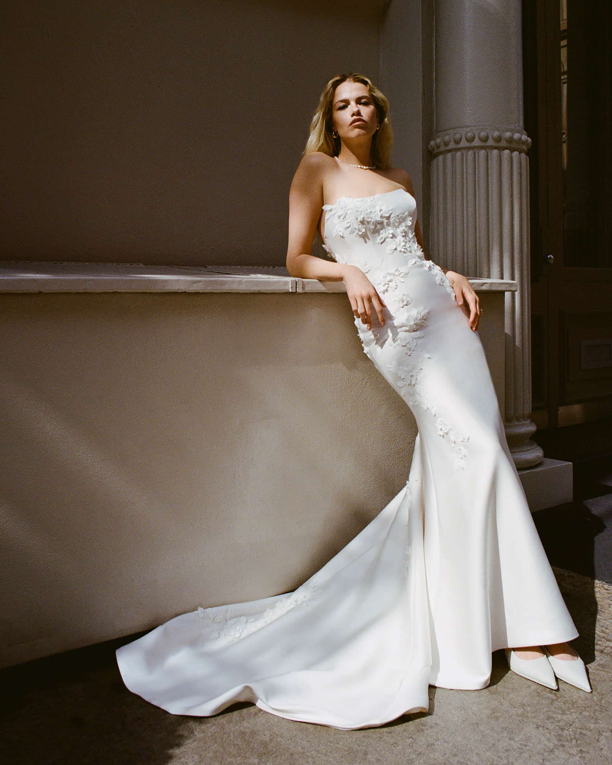 Bride with blonde hair wearing tight wedding dress leaning against a ledge