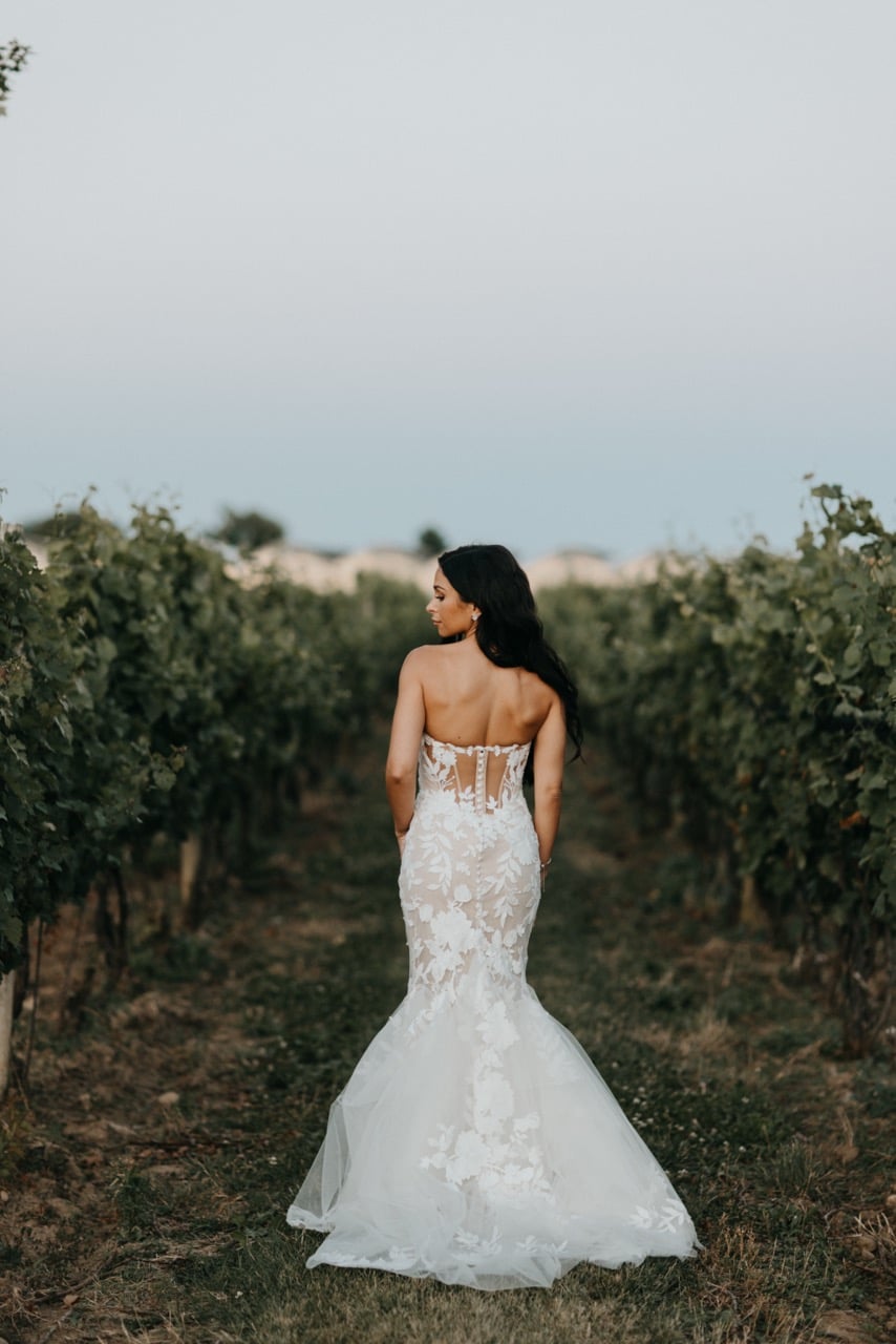 Bride standing in a field with mermaid style gown, viewed from the back